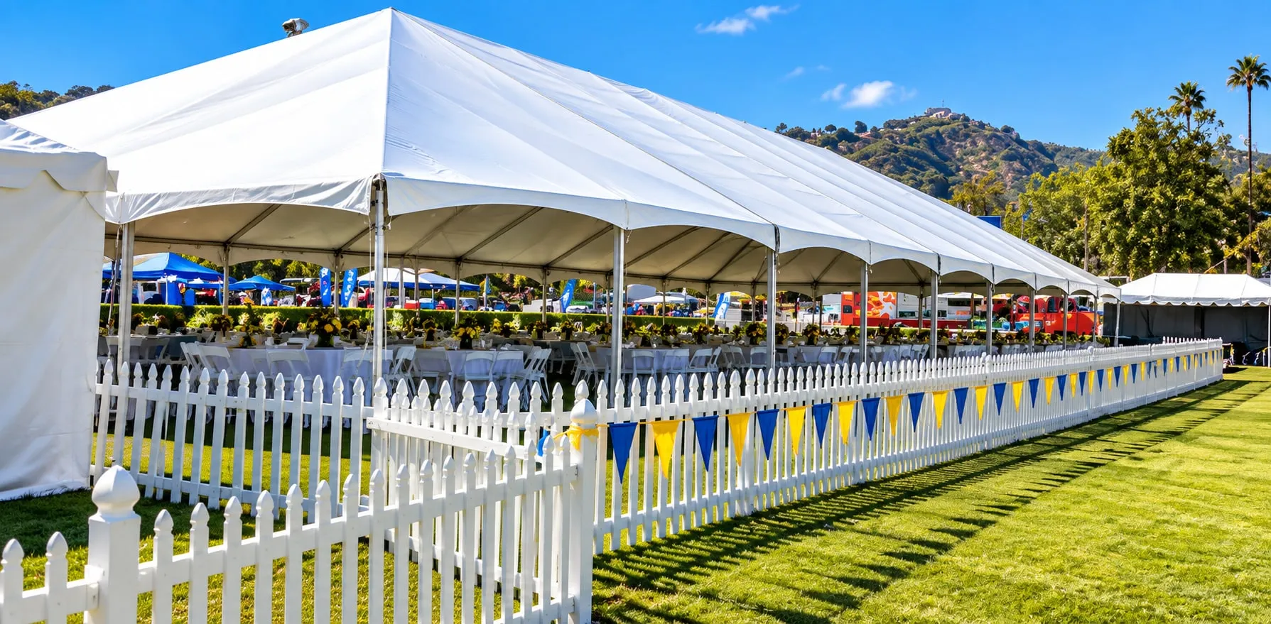 A long white clearspan structure running across an open field behind white perimeter fencing.