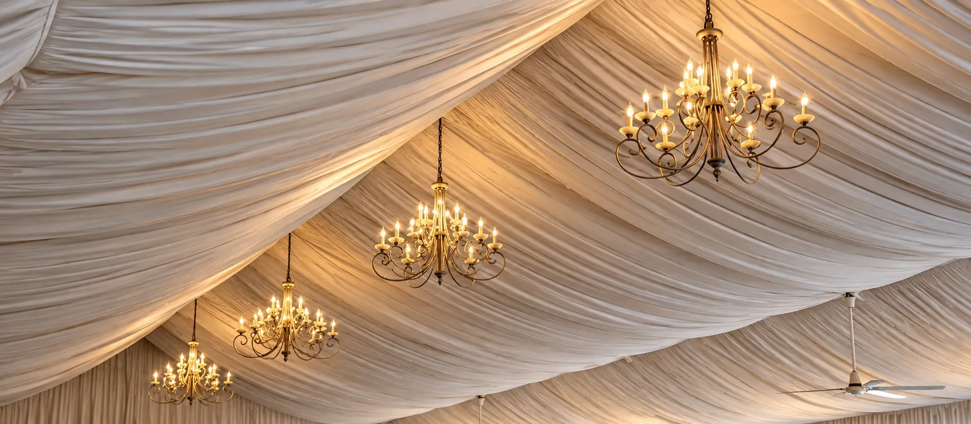 A draped tent ceiling with chandeliers suspended along its length.