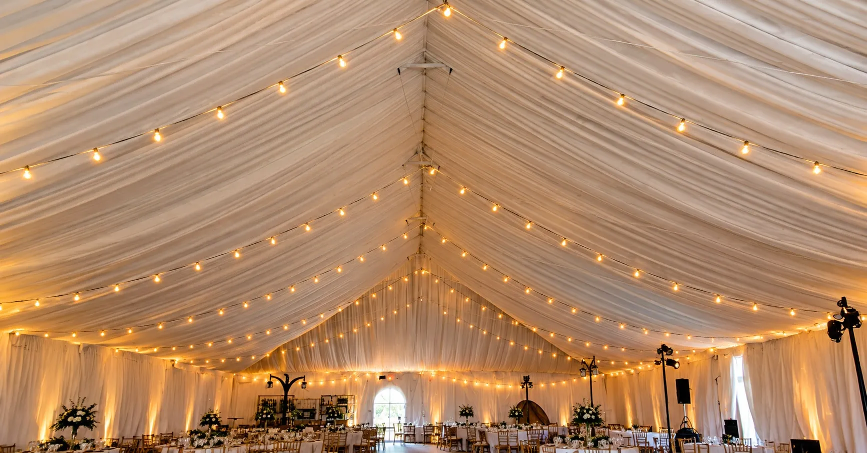 A draped tent interior with strings of festoon lights running the length of the ceiling.