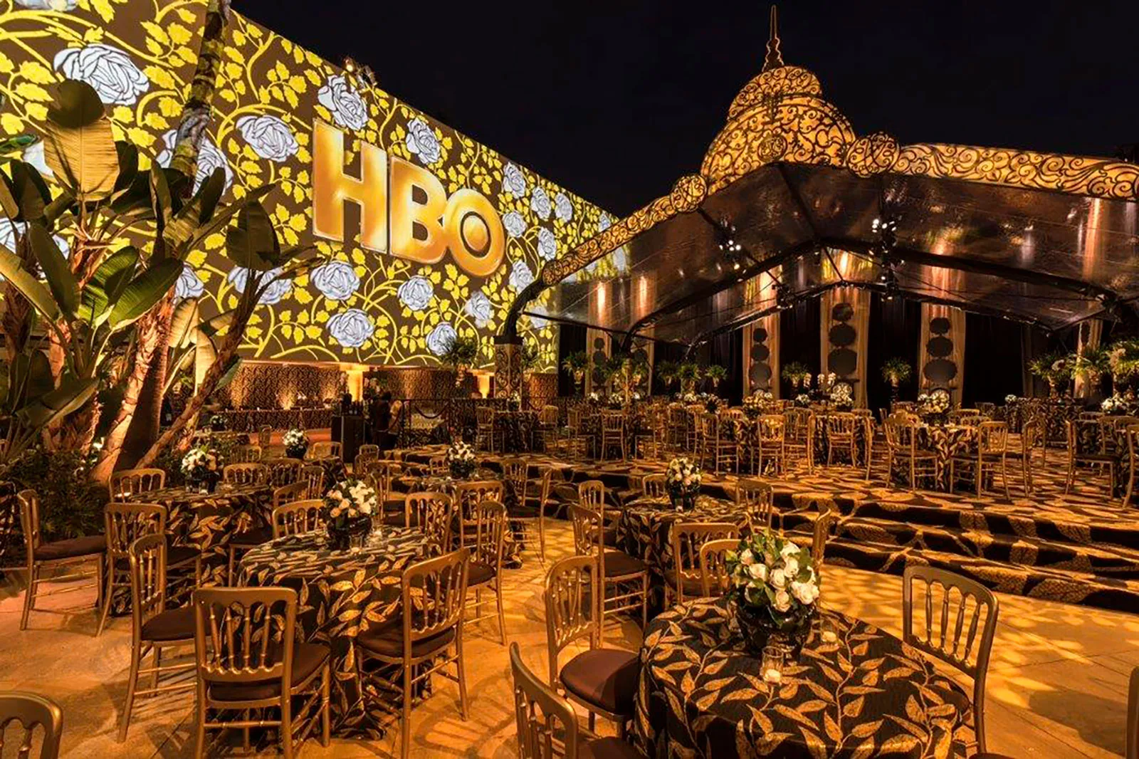 A banquet set beneath an ornately patterned illuminated ceiling at a night event, with signage on the structure behind.