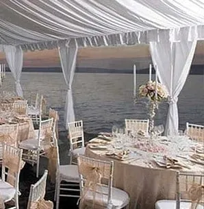 Tied-back white leg drapes on a tent at a waterfront reception.
