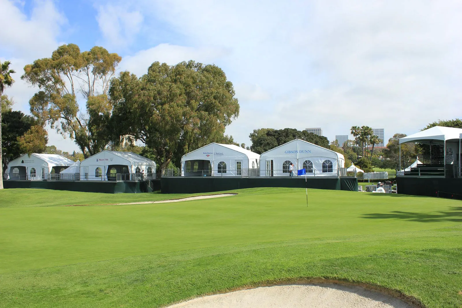A run of connected white frame tents set along a fairway.